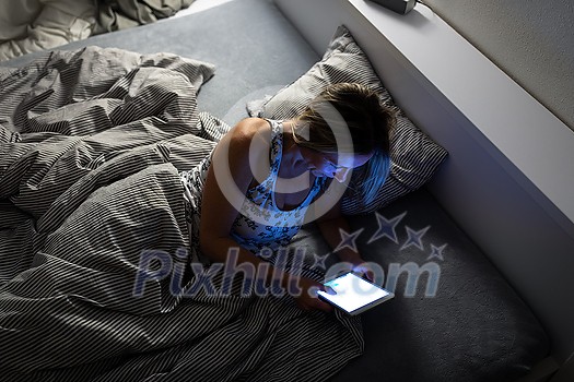 Pretty, middle-aged woman using her tablet computer before sleep in bed in the evening Pretty, middle-aged woman using her tablet computer before sleep in bed in the evening