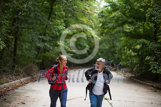 Active handsome senior walking, hiking outdoors on a forest path, enjoying his retirement with his daughter Active handsome senior walking, hiking outdoors on a forest path, enjoying his retirement with his daughter