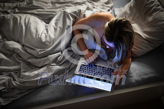 Pretty, middle-aged woman using her laptop computer before sleep in bed in the evening Pretty, middle-aged woman using her laptop computer before sleep in bed in the evening