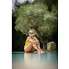 Young Beautiful Suntanned Woman wearing sunglasses relaxing next to a Swimming Pool  on a lovely Summer Day
