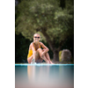 Young Beautiful Suntanned Woman wearing sunglasses relaxing next to a Swimming Pool  on a lovely Summer Day