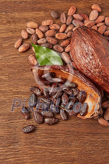 From above of whole and halved cocoa pods with pile of dark raw peeled and unpeeled cocoa beans on wooden surface From above of whole and halved cocoa pods with pile of dark raw peeled and unpeeled cocoa beans on wooden surface