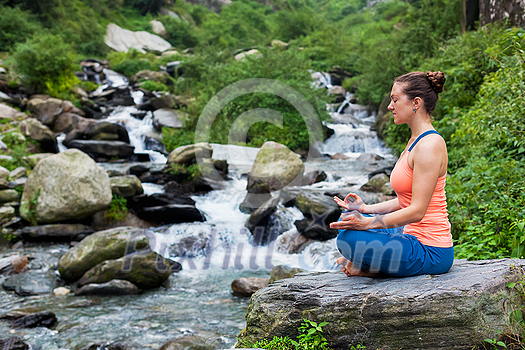 Woman meditating in Hatha yoga asana Padmasana outdoors at tropical waterfall Woman meditating in Hatha yoga asana Padmasana outdoors at tropical waterfall