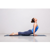 Woman doing Ashtanga Vinyasa yoga Surya Namaskar Sun Salutation asana Urdhva mukha svanasana - upward facing dog on yoga mat in studio on grey bagckground