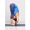 Woman doing Ashtanga Vinyasa yoga asana Padangusthasana - foot to fingers forward bend on yoga mat in studio on grey bagckground