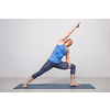 Woman doing Ashtanga Vinyasa yoga asana Utthita parsvakonasana - extended side angle pose beginner variation on yoga mat on yoga mat in studio on grey bagckground