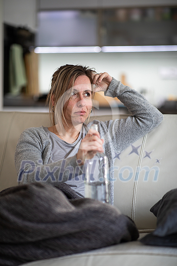 Midlle aged woman at home with a bottle of strong alcohol in her hands Midlle aged woman at home with a bottle of strong alcohol in her hands