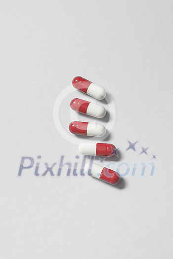 Red and white pharmaceutical pills laid over white background. Flat lay with copy space. Health care and medication-assisted treatment. Red and white pharmaceutical pills laid over white background. Flat lay with copy space. Health care and medication-assisted treatment.