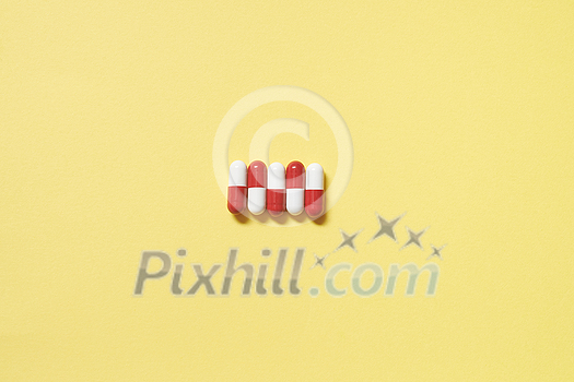 Red and white pharmaceutical capsules neatly laid over yellow backdrop, copy space. Health care and medication-assisted treatment. Red and white pharmaceutical capsules neatly laid over yellow backdrop, copy space. Health care and medication-assisted treatment.