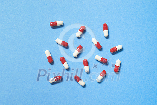 Red and white pharmaceutical capsules scattered over blue background, copy space. Health care and medication-assisted treatment. Red and white pharmaceutical capsules scattered over blue background, copy space. Health care and medication-assisted treatment.