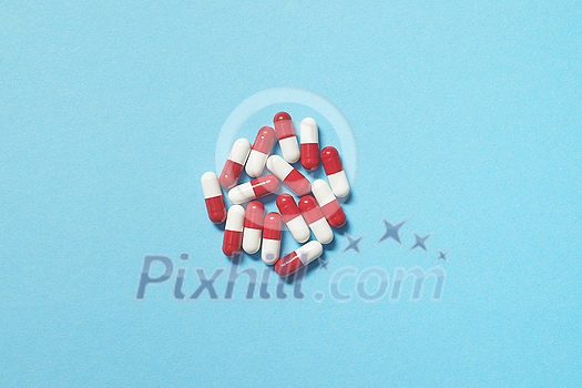 Red and white pharmaceutical tablets scattered over blue backdrop, copy space. Health care and medication-assisted treatment. Red and white pharmaceutical tablets scattered over blue backdrop, copy space. Health care and medication-assisted treatment.