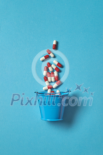 Pharmaceutical pills falling out of bucket over blue background. Top view with copy space. Pharmaceutical pills falling out of bucket over blue background. Top view with copy space.