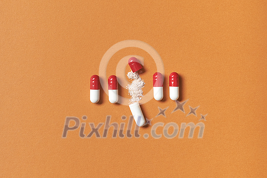Pharmaceutical capsules neatly laid with medication powder over orange background, top view. Pharmaceutical capsules neatly laid with medication powder over orange background, top view.