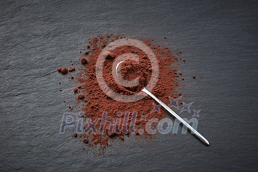 Top view of shiny spoon on piled of dark cocoa powder scattered on gray background Top view of shiny spoon on piled of dark cocoa powder scattered on gray background