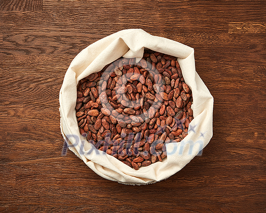 Top view of textile white bag filled with raw unpeeled cocoa beans placed on rustic wooden surface Top view of textile white bag filled with raw unpeeled cocoa beans placed on rustic wooden surface