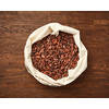 Top view of textile white bag filled with raw unpeeled cocoa beans placed on rustic wooden surface