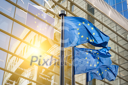 Flags of European Union against European Parliament office with sun light beam in Brussels, Belgium. Copy space for text on the left side