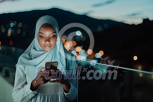 Young Muslim woman wearing scarf veil on urban city street at night texting on a smartphone with bokeh city light in the background. High-quality photo Young Muslim woman wearing scarf veil on urban city street at night texting on a smartphone with bokeh city light in the background. High-quality photo
