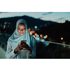 Young Muslim woman wearing scarf veil on urban city street at night texting on a smartphone with bokeh city light in the background. High-quality photo