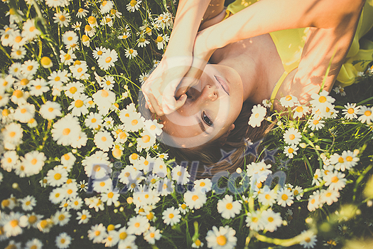 Portrait of young woman with radiant clean skin lying down amid flowers on a lovely meadow on a spring/summer day Portrait of young woman with radiant clean skin lying down amid flowers on a lovely meadow on a spring/summer day