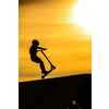 Silhouette of a young  boy riding a scooter against the background of a sea sunset