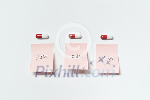 Red and white pharmaceutical pills and sticky notes with medication time over white background. Red and white pharmaceutical pills and sticky notes with medication time over white background.