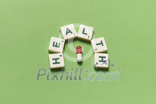 Health word formed of scrabble blocks and pharmaceutical pill over green background. Health and medical treatment concept. Health word formed of scrabble blocks and pharmaceutical pill over green background. Health and medical treatment concept.