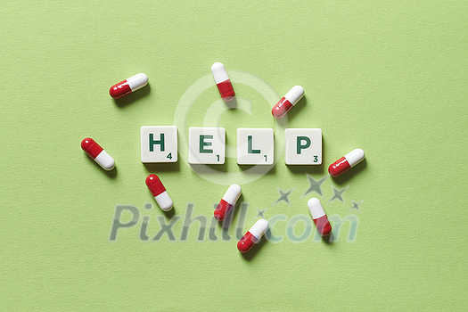Help word formed of scrabble blocks and pharmaceutical pills scattered over green backdrop. Health and medical treatment concept. Help word formed of scrabble blocks and pharmaceutical pills scattered over green backdrop. Health and medical treatment concept.