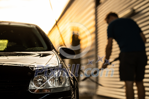 Young man washing his beloved car carefully in a manual car wash to prevent any damage and detail it properly Young man washing his beloved car carefully in a manual car wash to prevent any damage and detail it properly