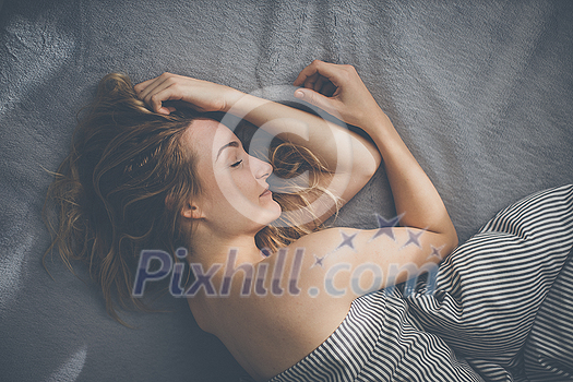 Pretty, young woman sleeping in her bed late in the morning on a weekend - compensating for the lack of sleep Pretty, young woman sleeping in her bed late in the morning on a weekend - compensating for the lack of sleep