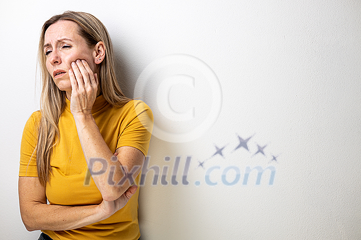 Mid-aged woman touching her cheek/mouth with painful expression because of toothache/dental issue Mid-aged woman touching her cheek/mouth with painful expression because of toothache/dental issue