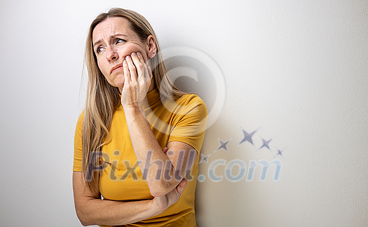 Mid-aged woman touching her cheek/mouth with painful expression because of toothache/dental issue Mid-aged woman touching her cheek/mouth with painful expression because of toothache/dental issue