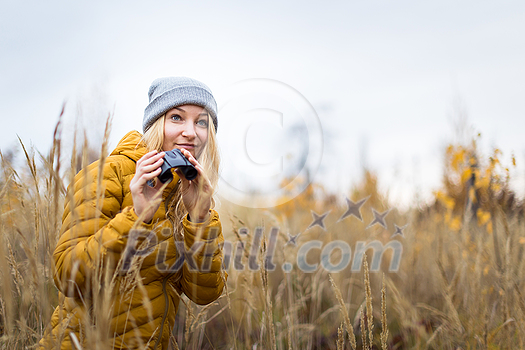 Young woman with binoculars outdoors on fall day. Enjoying the outdoors.