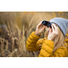 Young woman with binoculars outdoors on fall day. Enjoying the outdoors.