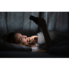 Young woman in bed holding a phone, tired and exhausted, blue light straining her eyes, messing up her circadian rhytm