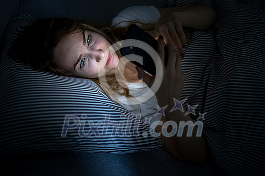 Young woman in bed holding a phone, tired and exhausted, blue light straining her eyes, messing up her circadian rhytm Young woman in bed holding a phone, tired and exhausted, blue light straining her eyes, messing up her circadian rhytm