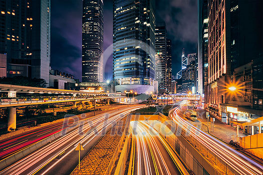 Street traffic in Hong Kong at night. Office skyscraper buildings and busy traffic on highway road with blurred cars light trails. Hong Kong, China