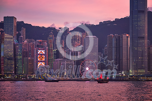 Tourist junk boat ferry with red sails and Hong Kong skyline cityscape downtown skyscrapers over Victoria Harbour in the evening. Hong Kong, China