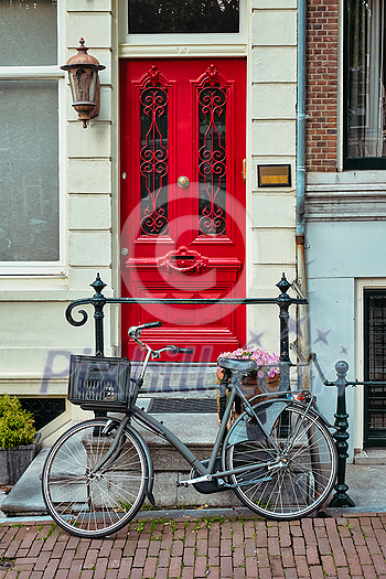 Bicycle near door of old house in Amsterdam street. Bicycles are the very popular means of transport in Netherlands. Amsterdam, Netherlands Bicycle near door of old house in Amsterdam street. Bicycles are the very popular means of transport in Netherlands. Amsterdam, Netherlands