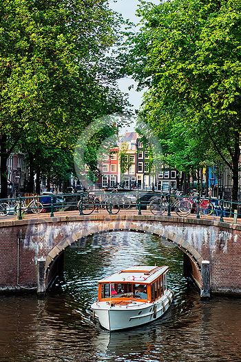 Amsterdam view - canal with boat passing under bridge and old houses. Amsterdam, Netherlands Amsterdam view - canal with boat passing under bridge and old houses. Amsterdam, Netherlands