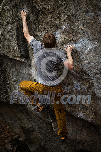 A rock climber climbing on a boulder rock outdoors. Group of friends involved in sports outside. A rock climber climbing on a boulder rock outdoors. Group of friends involved in sports outside.