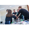 Group of young students in electronics classroom celebrating successfully finished project with holding their hands together, education and technology concept