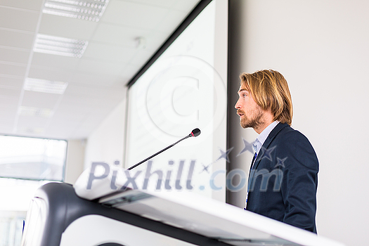 Handsome young man giving a speech at a conference Handsome young man giving a speech at a conference