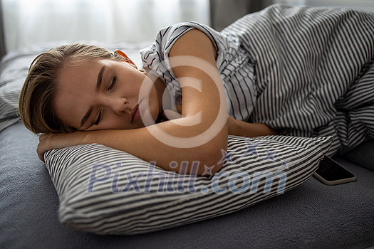Pretty, young woman sleeping in her bed with her cell phone close to her. Smartphone in Bed Mobile/smartphone Addiction Concept. Pretty, young woman sleeping in her bed with her cell phone close to her. Smartphone in Bed Mobile/smartphone Addiction Concept.