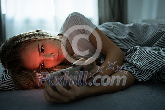 Pretty, young woman sleeping in her bed with her cell phone close to her. Smartphone in Bed Mobile/smartphone Addiction Concept. Pretty, young woman sleeping in her bed with her cell phone close to her. Smartphone in Bed Mobile/smartphone Addiction Concept.