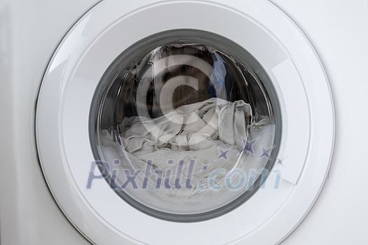 Close-up laundry running washing machine at home, amid a washing cycle, home electronics concept Close-up laundry running washing machine at home, amid a washing cycle, home electronics concept