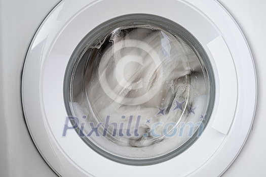 Close-up laundry running washing machine at home, amid a washing cycle, home electronics concept Close-up laundry running washing machine at home, amid a washing cycle, home electronics concept