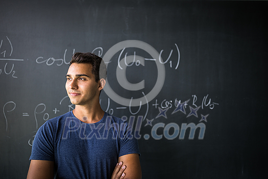 Students in a classroom - handsome student solving a math problem on a blackboard during math class Students in a classroom - handsome student solving a math problem on a blackboard during math class