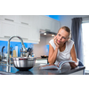 Pretty, young woman in her modern, clean and bright kitchen, uncertain about what to cook (color toned imagey; shallow DOF)