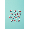 Red and white pharmaceutical pills strewn over turquoise backdrop. Flat lay with copy space.